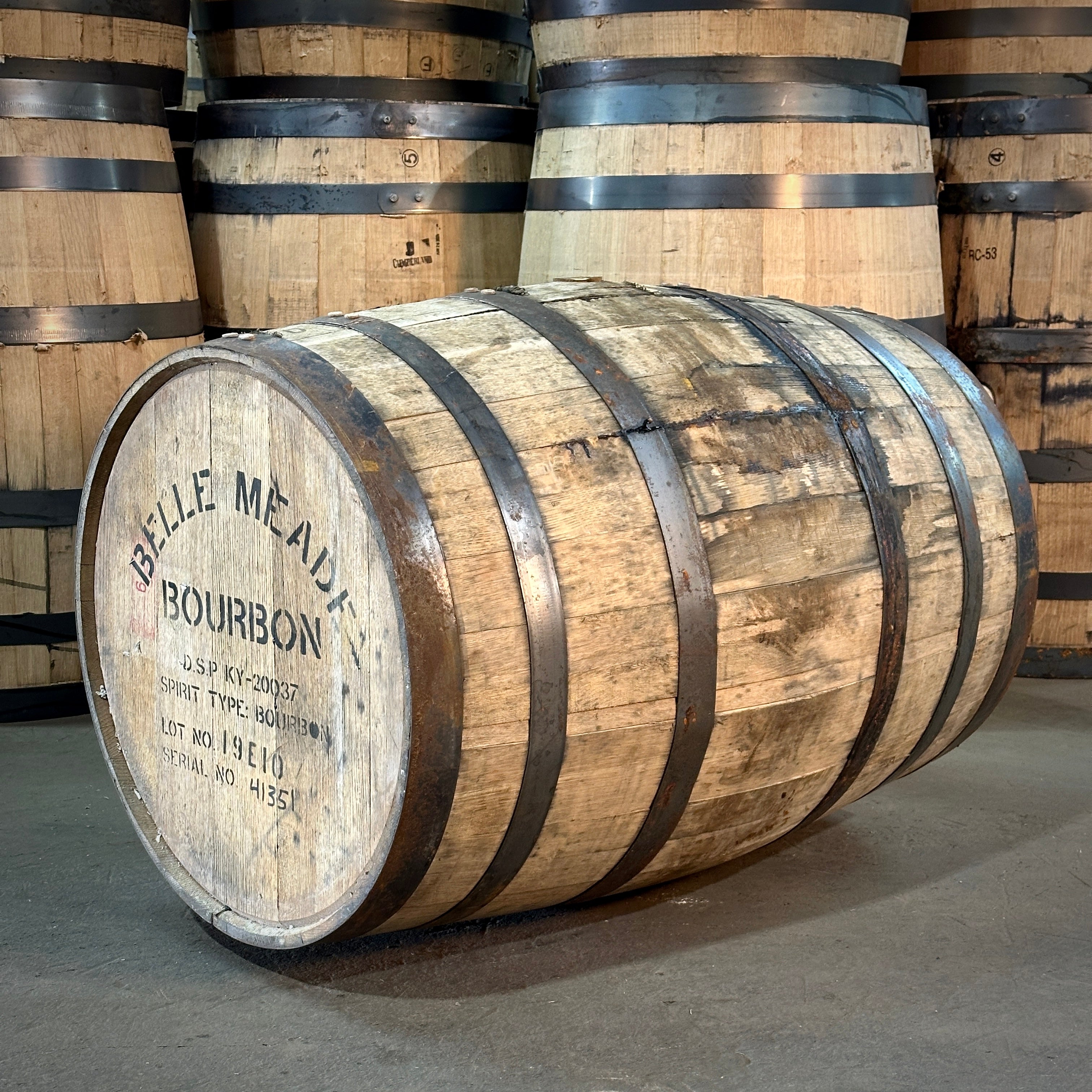 A Belle Meade Bourbon barrel with visible branding, situated in a warehouse setting with other barrels in the background.