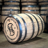 Wooden barrel with branding and text Salt Lake City Utah Sugar House Distillery stacked with other barrels in the background.