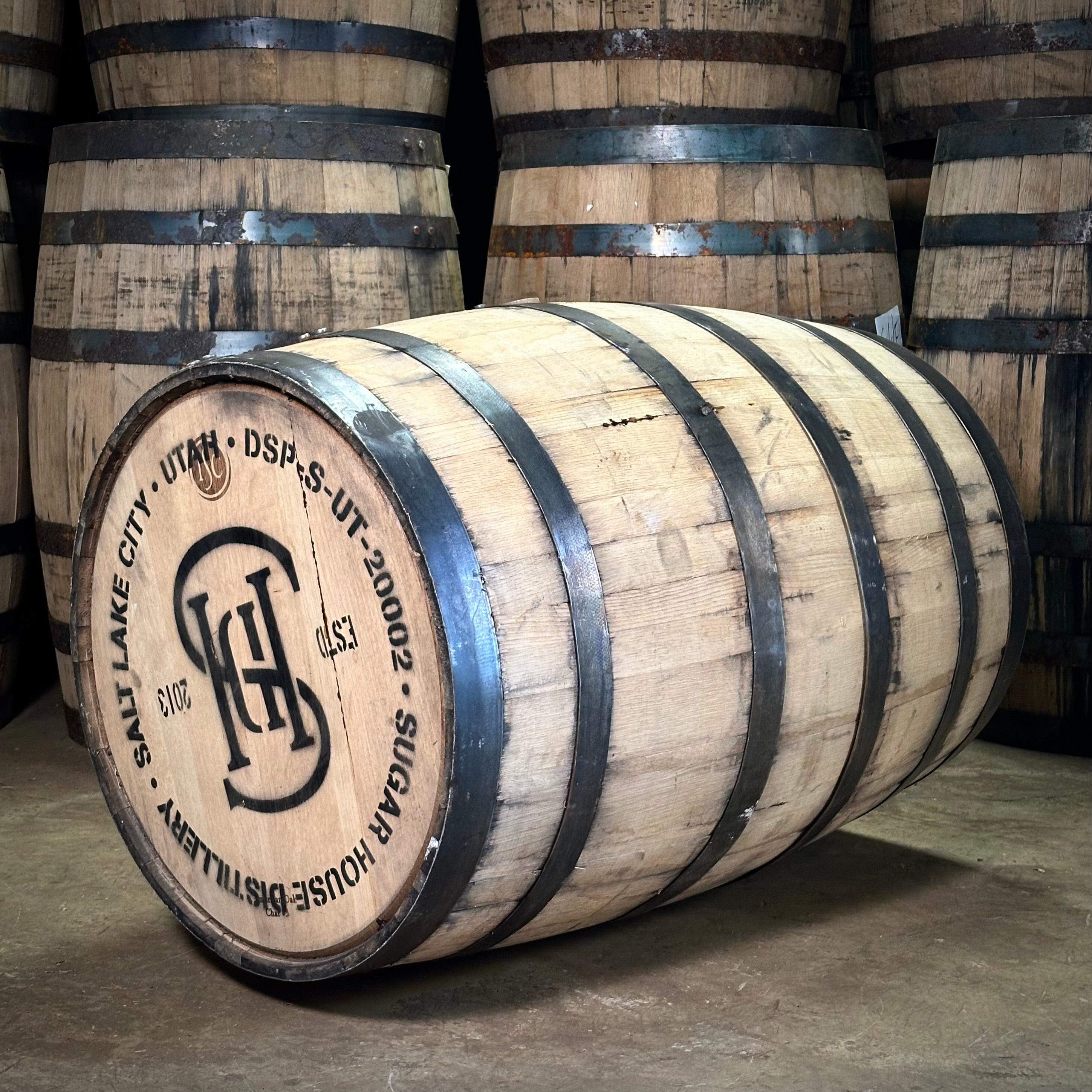Wooden barrel with branding and text Salt Lake City Utah Sugar House Distillery stacked with other barrels in the background.