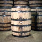 Wooden barrels with metal bands stacked together on a concrete floor.