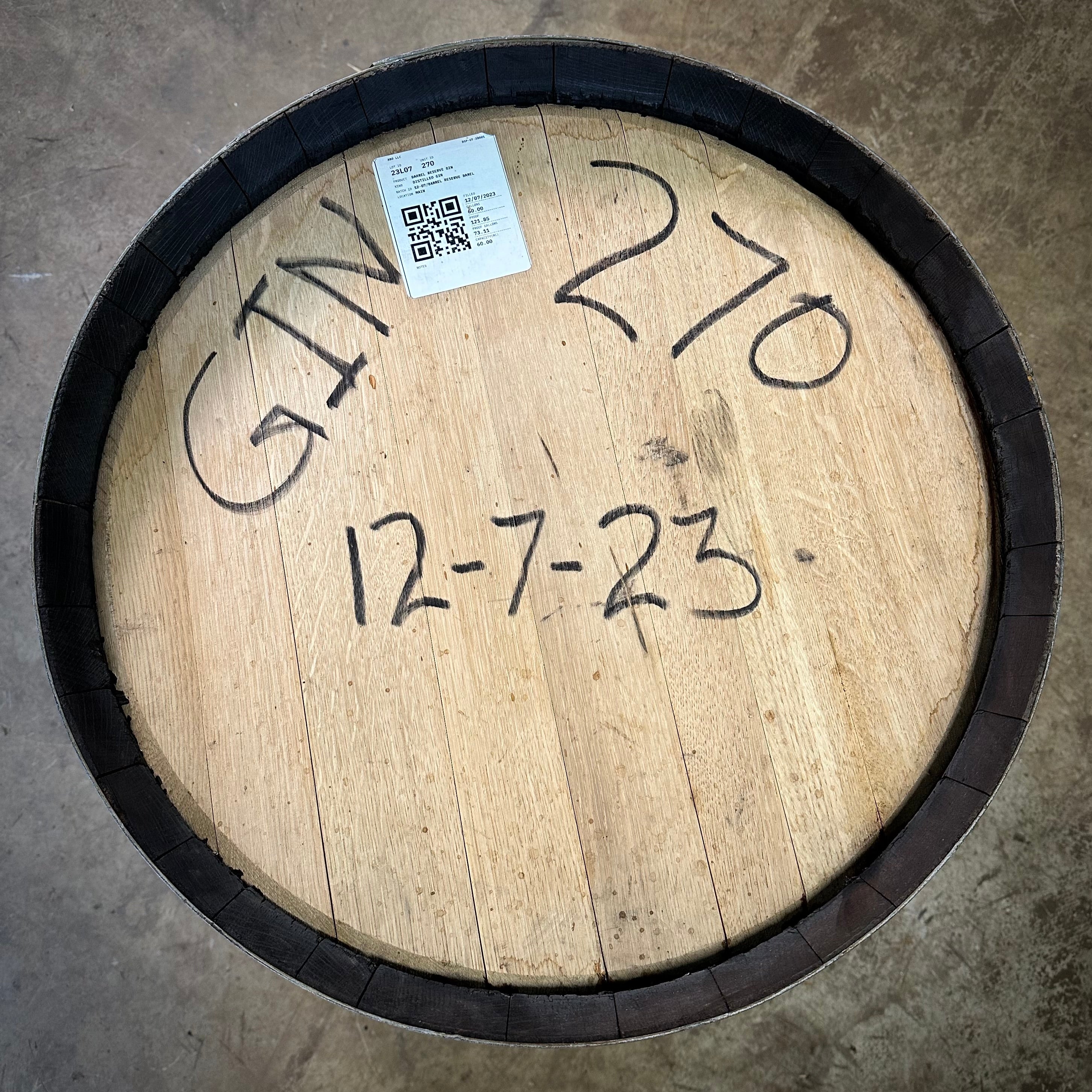 Wooden barrel with handwritten numbers and a QR code label on a concrete floor.