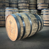 Wooden whiskey barrels with visible branding of Treaty Oak Bourbon Whiskey on a dark floor